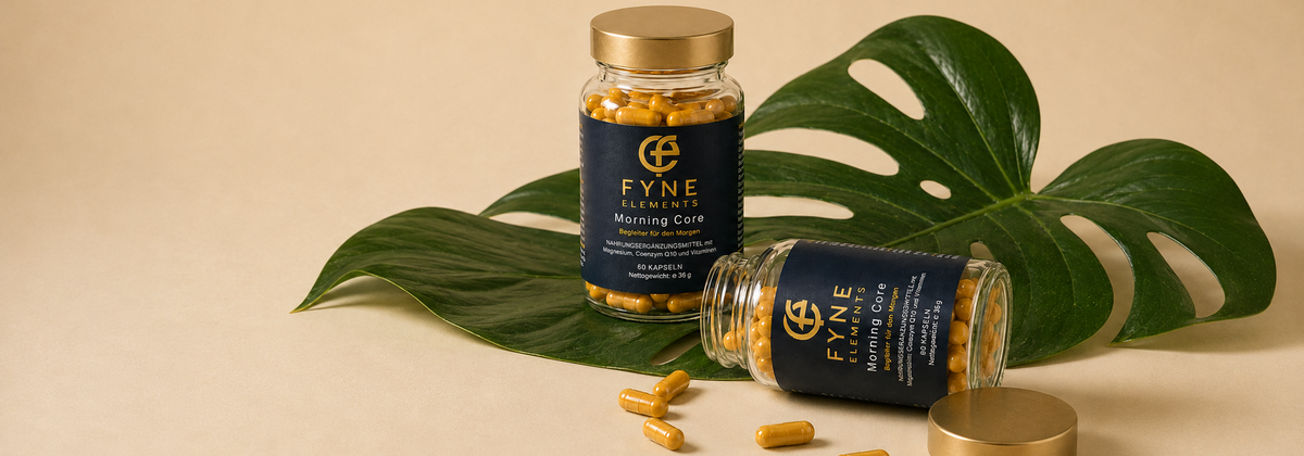 Zwei Gläser Fyne Elements Morning Core mit gelben Kapseln und goldfarbenen Deckeln vor grünen Monstera Blättern.